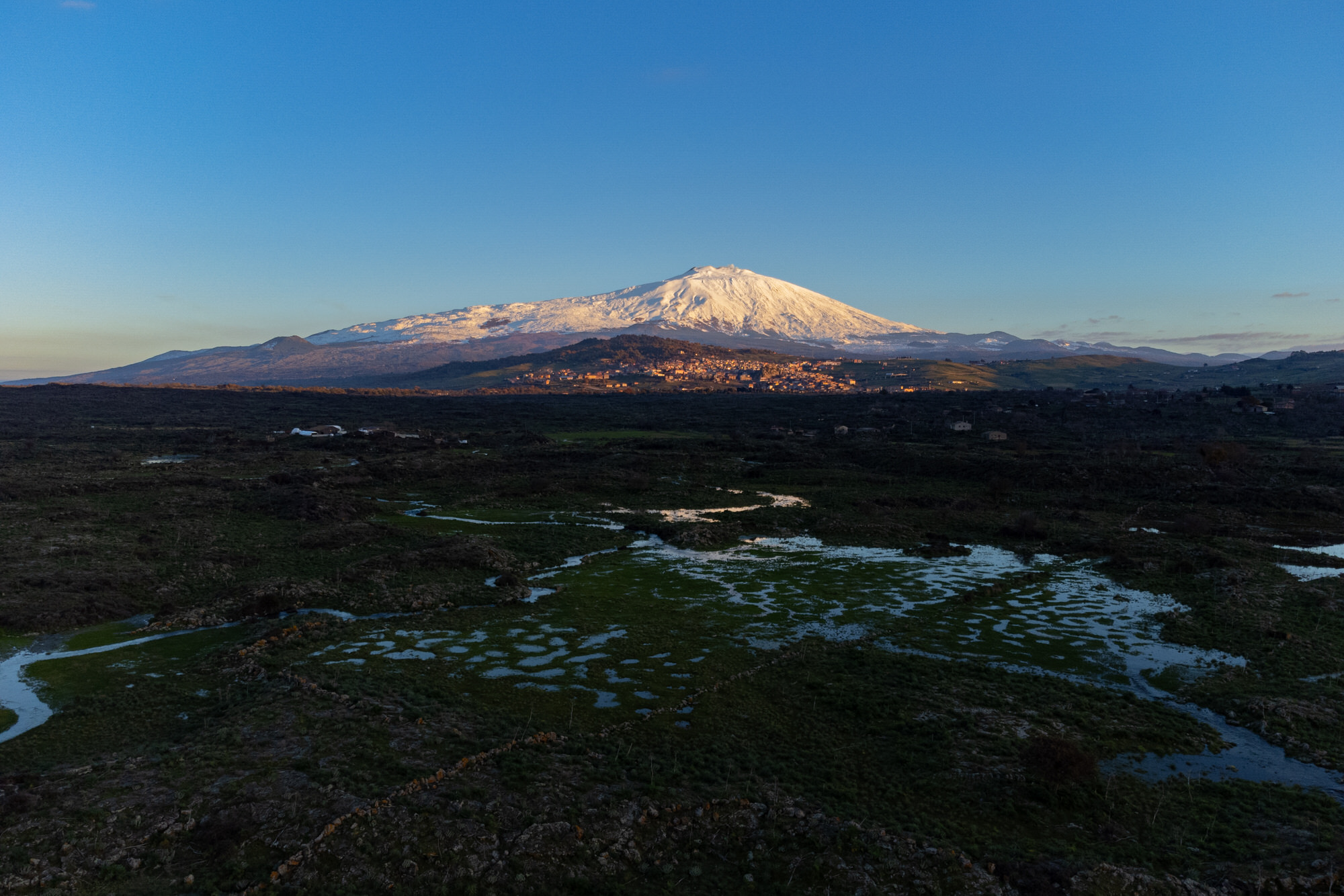Bronte town under the snowy and majestic volcano Etna and a cloudy blue sky Bronte town under the snowy and majestic volcano Etna and a cloudy blue sky